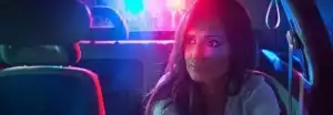 A woman sits in her car at night, illuminated by red and blue lights, exuding the quiet confidence of an attorney.