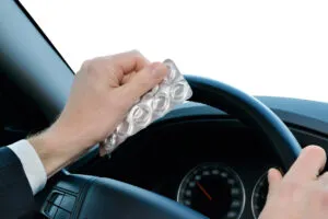 A person holding an empty blister pack of prescription drugs while steering a car, navigating the road with careful attention.