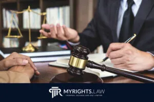 Dos personas vestidas de gala discuten asuntos legales en un escritorio con un mazo, una balanza de la justicia y papeleo. El logotipo 