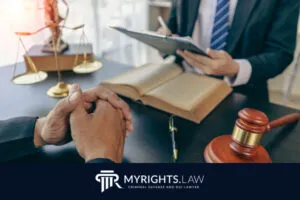 Dos personas se reúnen en un escritorio con documentos legales, un mazo y una balanza de la justicia; una toma notas mientras la otra escucha. El logotipo