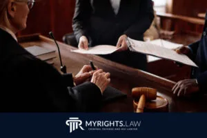 Un juez de Los Ángeles revisa documentos entregados por dos personas en una sala del tribunal, con un mazo y un bloque de sonido visibles en el escritorio, ideal para un abogado de delitos menores que busca justicia.