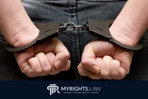 Se muestra a una persona en jeans de espaldas con las manos esposadas con esposas metálicas. La imagen muestra el logotipo de MyRights.Law de defensa penal y el de Abogado de Delitos Menores de Los Ángeles en la parte inferior.
