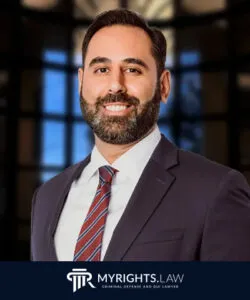 Un hombre con traje y corbata se encuentra frente a un fondo borroso en San Bernardino, con el logotipo de MyRights.Law de defensa penal, abogado de delitos sexuales y abogado de DUI mostrado en la parte inferior.