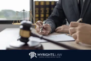 Dos personas de traje se sientan en un escritorio en San Bernardino, revisando documentos legales con un mazo, una balanza de justicia y libros de leyes cerca, representando a MYRIGHTS.LAW, servicios de abogados con experiencia en delitos sexuales.