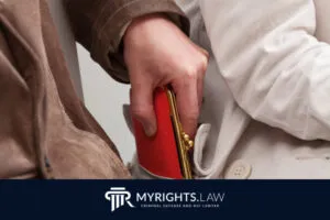 Una persona roba una billetera roja del bolsillo de un abrigo ajeno. El logo y el texto en la parte inferior dicen: