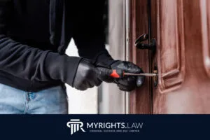 Person wearing gloves using a screwdriver to pry open a door lock, with a MyRights.Law banner at the bottom, emphasizing the importance of consulting a Los Angeles Misdemeanor Lawyer for such cases.