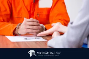 Persona con uniforme de prisión naranja y esposas sentada en una mesa con un abogado de delitos sexuales de San Bernardino, discutiendo papeleo. 