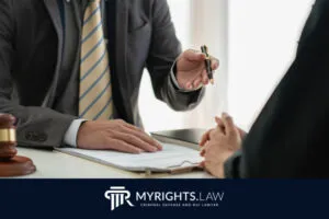 Dos personas se sientan en un escritorio discutiendo documentos legales, una sostiene un bolígrafo. Un mazo y 