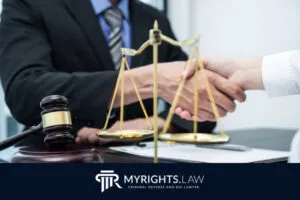 Dos personas vestidas de negocios se dan la mano en un escritorio con un mazo, documentos legales y una balanza de la justicia, que simbolizan ayuda legal confiable; el logotipo de MYRIGHTS.LAW es visible en la parte inferior.