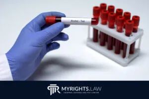 A gloved hand holds a blood sample tube labeled 