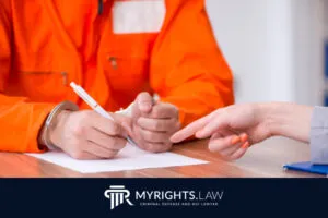 A person in an orange jumpsuit and handcuffs signs a document while another points at the paper. The MYRIGHTS.LAW logo is visible at the bottom, highlighting trusted Riverside Criminal Defense Attorney services.