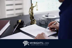 A person reviews a contract at a desk with a gavel, Lady Justice statue, glasses, and large book—studying the difference between DUI and DWI; a computer monitor sits in the background.