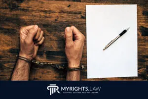 A person in handcuffs sits at a wooden table with a blank sheet of paper and a pen, suggesting a serious felony case; a California law firm's logo and name appear at the bottom of the image.