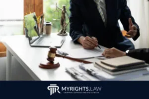 Two people in business attire discuss legal documents about the difference between DWI and DUI at a desk with a gavel, Lady Justice statue, laptop, and files. 