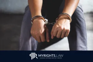 Una persona sentada con las manos esposadas al frente, vestida con ropa informal, simboliza los desafíos que supone que un delito menor quede en el expediente. El logotipo y el eslogan de MyRights.Law aparecen en la parte inferior.