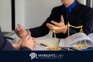 Dos personas trajeadas conversan en un escritorio con libros de derecho y una balanza de justicia, destacando la Defensa Penal de Santa Ana. El logotipo de MyRights.Law y el texto "Abogado de Defensa Penal y DUI" aparecen en la parte inferior.