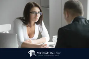 Una mujer con gafas toma notas mientras escucha a un hombre al otro lado de la mesa en un entorno de oficina, discutiendo cómo un DUI podría afectar mi trabajo; el logotipo de MyRights.Law se muestra en la parte inferior.