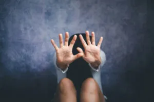 A person sits with knees drawn up, raising both hands with open palms toward the camera, against a dark textured background—capturing a moment that echoes the gravity of domestic violence in California.