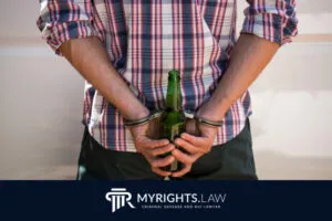 Una persona esposada sostiene una botella de cerveza verde a la espalda. El logotipo y el texto... 