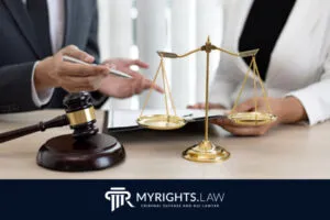 Dos personas discuten documentos legales en un escritorio, con un mazo y una balanza de la justicia en primer plano, analizando cuánto tiempo permanece un delito menor en el expediente. El logotipo en la parte inferior dice 