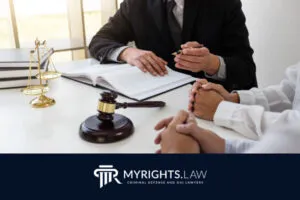 Dos personas se sientan frente a un abogado defensor penal de Orange en un escritorio con documentos legales, un mazo y una balanza de justicia; el logotipo de MyRights.Law aparece en la parte inferior.