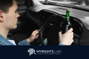 A person sits in the driver’s seat of a car, holding a bottle of beer in one hand and car keys in the other. The logo 