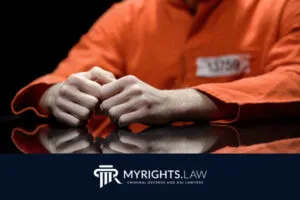 Person in an orange prison jumpsuit with hands resting on a table; partial inmate ID visible. Logo below reads “MYRIGHTS.LAW Burbank Criminal Defense and DUI Attorney.”.