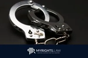 A pair of metal handcuffs rests on a dark surface above a logo for MyRights.Law, a Glendale criminal defense attorney firm.
