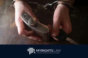A person in handcuffs holds a metal flask and car key over a wooden surface, with a 