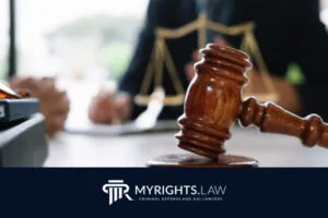 Un mazo de juez y una balanza de justicia sobre un escritorio, con figuras borrosas en el fondo; el logotipo de MyRights.Law Attorney en la parte inferior, destacando los servicios confiables de Defensa Penal en Hesperia.
