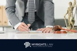 A Glendale attorney in a suit signs documents at a desk with a gavel, scales of justice, and the MyRights.Law logo displayed at the bottom, emphasizing expert criminal defense services.