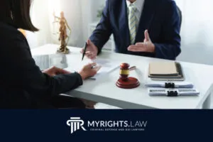 Two people sit at a desk in Highland with legal documents, a gavel, and a Lady Justice statue; an attorney explains while the other takes notes. 