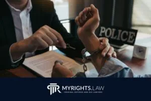 Una persona esposada se sienta a una mesa mientras un abogado penalista de Ontario le abre las esposas. Se ven un cartel policial y documentos legales. El logotipo de MyRights.Law está en la parte inferior.