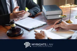 Dos personas se sientan a una mesa con documentos legales, un mazo, libros de leyes y una balanza de la justicia. Una toma notas mientras la otra gesticula. El texto dice: 