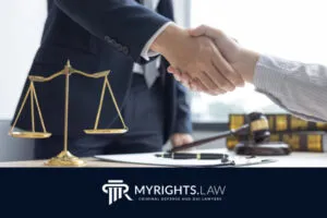 Dos personas se dan la mano sobre un escritorio con libros de derecho, una balanza, un mazo y documentos. El logo en la parte inferior dice: 