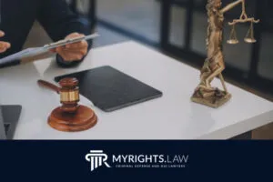 Una persona revisa documentos en un escritorio con un mazo, una tableta, una computadora portátil y una estatua de Lady Justice, sobre un logotipo que dice 