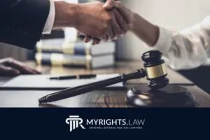 Dos personas se dan la mano sobre un escritorio con documentos legales, un mazo y libros, indicando un acuerdo legal o una consulta con un abogado penalista de Lancaster. El logotipo de MyRights.Law es visible en la parte inferior.