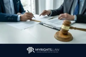 Two people in suits sit at a desk with legal documents, a pen, a wooden gavel, and a book, highlighting the expertise of your Corona Criminal Defense Attorney. The MyRights.Law logo and tagline appear at the bottom.