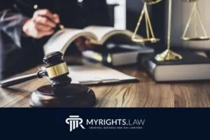 A judge's gavel, legal books, and scales of justice on a desk, with a person writing in the background; MyRights.Law branding highlights trusted Garden Grove Criminal Defense Attorney services.
