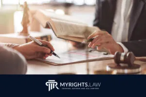 Two people sit at a desk discussing documents; one holds a pen, the other gestures with a book. A gavel and legal paperwork are visible, reflecting the expertise of a Rancho Cucamonga Bribery Lawyer. The logo 