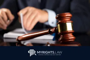 A wooden gavel rests on a desk in front of a person flipping through documents; logo and text read 
