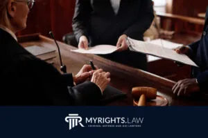 A judge reviews documents handed over by two people in a courtroom. A gavel and paperwork are visible on the desk. The image features the MyRights.Law logo at the bottom, highlighting a Rancho Cucamonga CACI Removal Lawyer’s expertise.