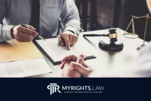 Two people sit at a desk reviewing legal documents, with a gavel, scales of justice, and 