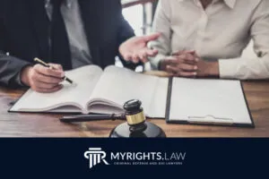 Two people sit at a desk with legal documents, a clipboard, and a judge’s gavel. The image features the MYRIGHTS.LAW Criminal Defense and DUI Lawyers logo, highlighting their expertise as a Rancho Cucamonga Bribery Lawyer.