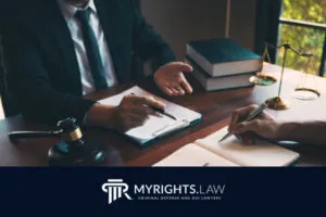 Two people sit at a desk with legal documents, a gavel, scales of justice, and books; one gestures while the other takes notes. The MyRights.Law logo is displayed below, highlighting trusted Rancho Cucamonga Bribery Lawyer services.