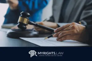 A person signing a document next to a wooden gavel with another individual in the background; 