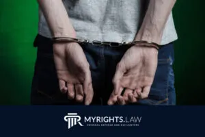 A person in jeans and a gray shirt is shown from behind with hands cuffed, above a logo that reads 