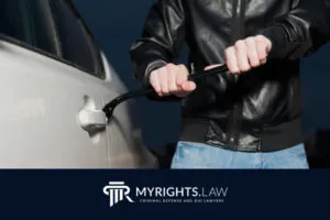 Person in a black jacket using a crowbar to pry open a car door, with the MyRights.Law criminal defense, DUI lawyers, and Rancho Cucamonga Bribery Lawyer logo at the bottom.