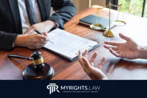 Two people sit at a desk discussing documents with a gavel and scales of justice visible; 